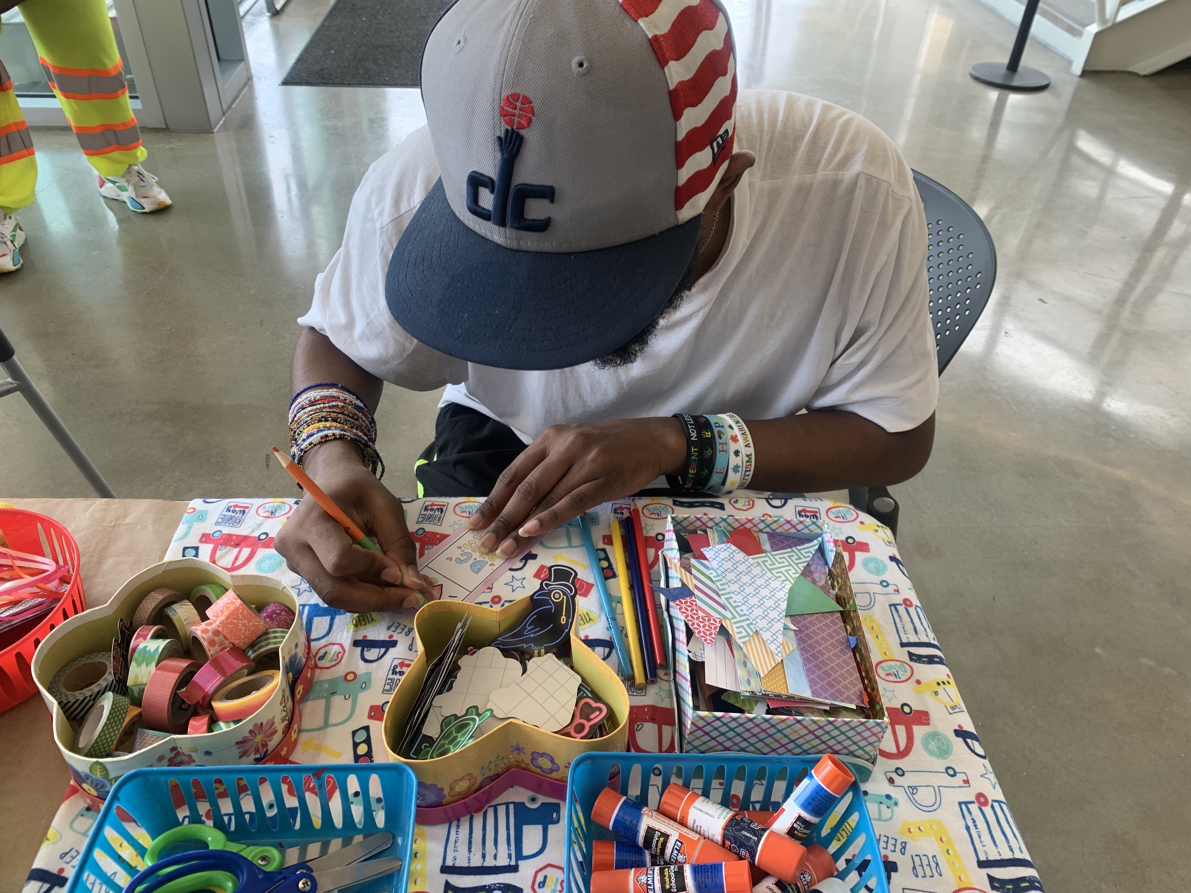 Person sitting down and coloring. Lots of craft supplies on desk like scissors, glue, and tape.