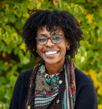 Woman with glasses standing in front of bushes smiling 