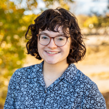 Girl with short hair and glasses standing outside smiling