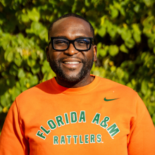 Man in orange sweatshirt smiling against a green nature background