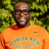 Man in orange sweatshirt smiling against a green nature background